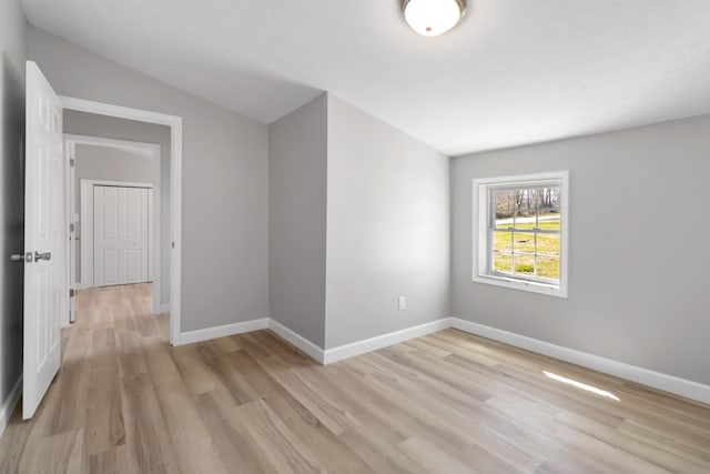empty room with baseboards, light wood-type flooring, and lofted ceiling