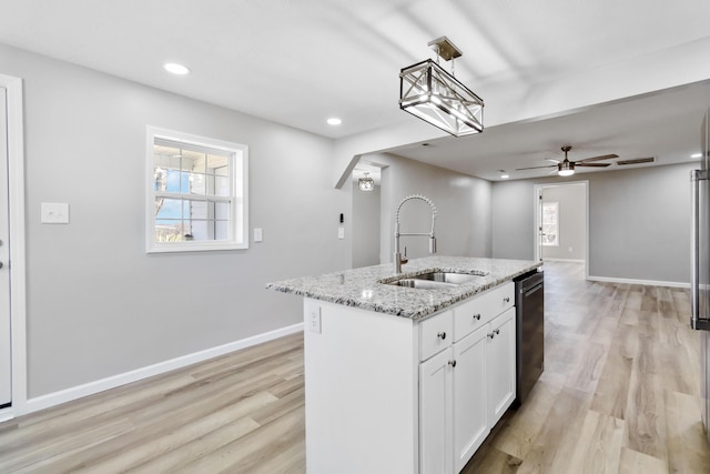 kitchen with baseboards, light stone counters, dishwashing machine, light wood finished floors, and a sink