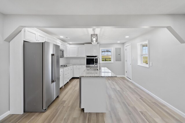 kitchen with a kitchen island with sink, white cabinetry, light stone countertops, light wood-style flooring, and stainless steel appliances