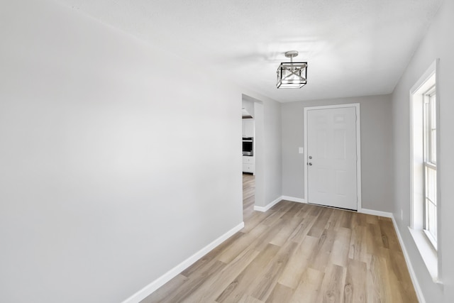 interior space featuring baseboards, light wood-type flooring, and a notable chandelier