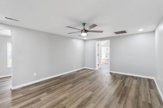 empty room with wood finished floors, baseboards, a ceiling fan, and visible vents