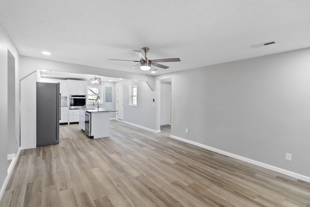 unfurnished living room with visible vents, baseboards, a sink, a ceiling fan, and light wood-style flooring