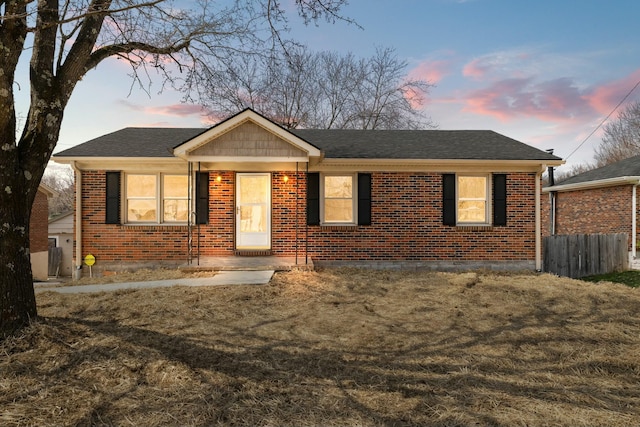 view of front of home featuring brick siding, fence, and roof with shingles