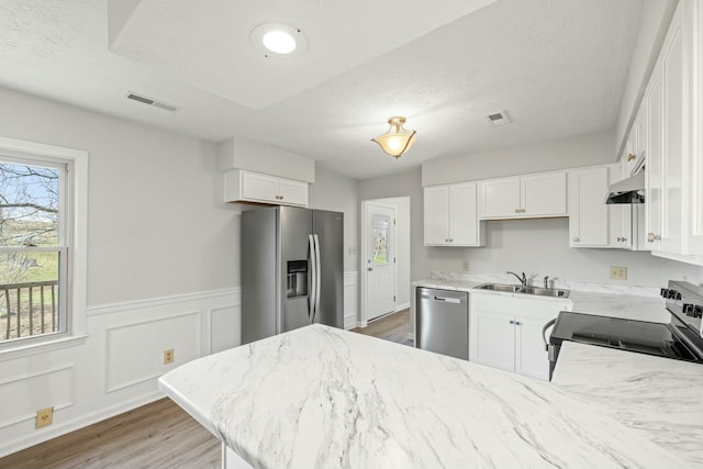 kitchen featuring a sink, appliances with stainless steel finishes, a peninsula, under cabinet range hood, and visible vents