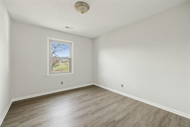 spare room featuring wood finished floors, a textured ceiling, baseboards, and visible vents