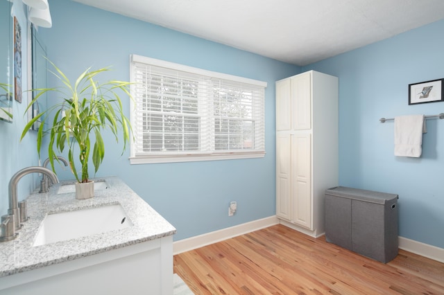 bathroom with baseboards, double vanity, a sink, and wood finished floors