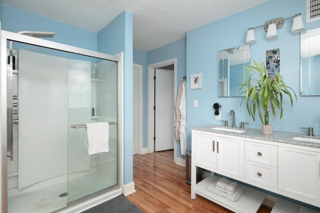bathroom with double vanity, a sink, a stall shower, and wood finished floors