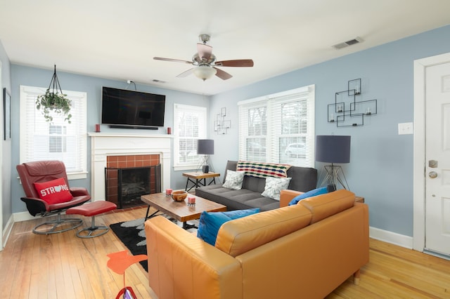 living room with visible vents, baseboards, ceiling fan, a tiled fireplace, and hardwood / wood-style floors