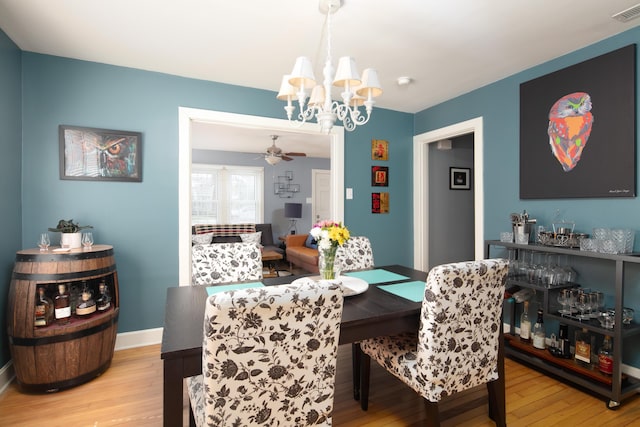 dining room with baseboards, visible vents, wood finished floors, and ceiling fan with notable chandelier