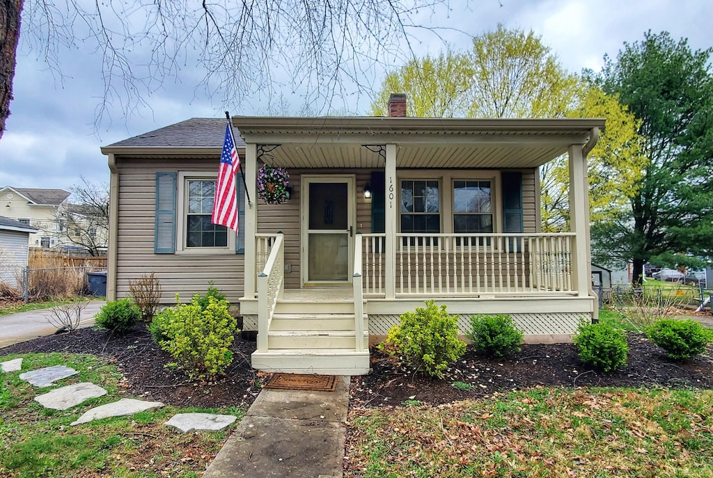 bungalow-style house featuring a chimney, covered porch, and fence