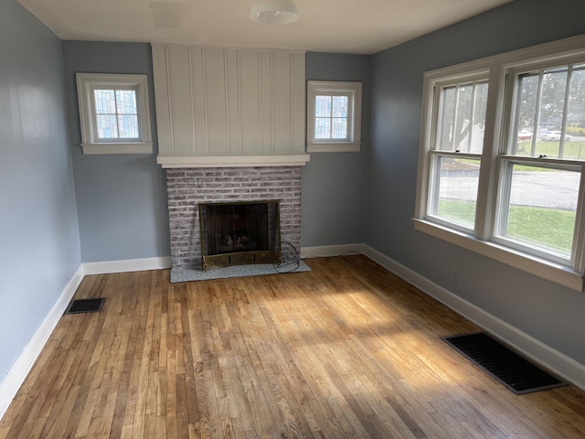 unfurnished living room featuring baseboards, hardwood / wood-style flooring, visible vents, and a fireplace