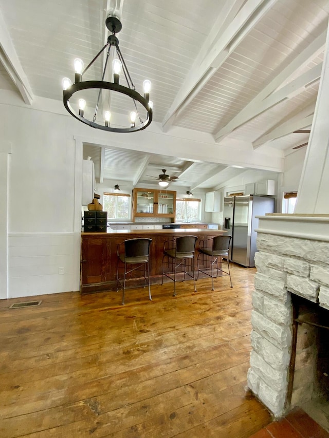 kitchen with stainless steel fridge, lofted ceiling with beams, ceiling fan with notable chandelier, a breakfast bar, and hardwood / wood-style flooring