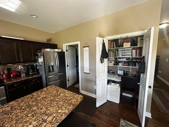 kitchen featuring dark stone counters, dark brown cabinets, baseboards, and stainless steel fridge