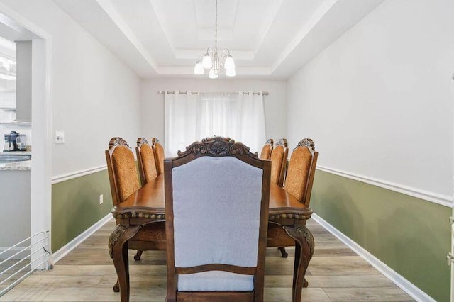 dining area featuring a tray ceiling, baseboards, light wood-style floors, and a chandelier