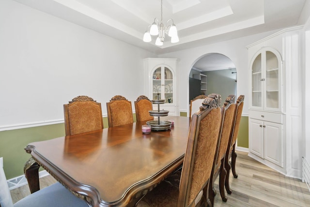 dining room with light wood-type flooring, an inviting chandelier, baseboards, a raised ceiling, and arched walkways