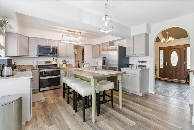 kitchen with a kitchen island with sink, arched walkways, appliances with stainless steel finishes, and light wood-type flooring
