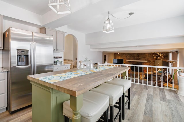 kitchen with stainless steel fridge with ice dispenser, arched walkways, light wood-style flooring, and wooden counters
