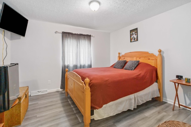 bedroom featuring baseboards, a textured ceiling, visible vents, and wood finished floors