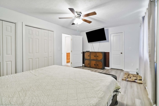 bedroom with multiple closets, a textured ceiling, baseboards, a ceiling fan, and light wood-type flooring