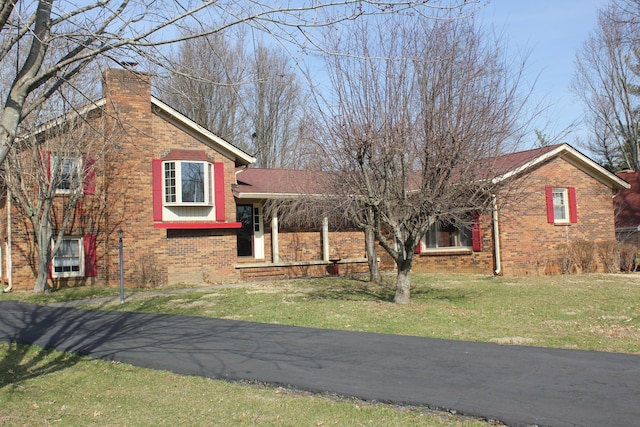view of front of house featuring brick siding, a front yard, and a chimney