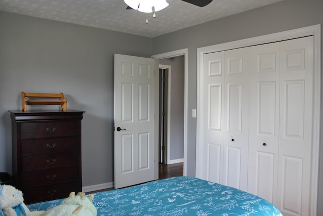 bedroom featuring a closet, a textured ceiling, baseboards, wood finished floors, and a ceiling fan