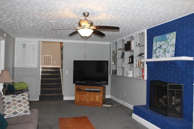 carpeted living area featuring a textured ceiling, crown molding, stairs, a fireplace, and a ceiling fan