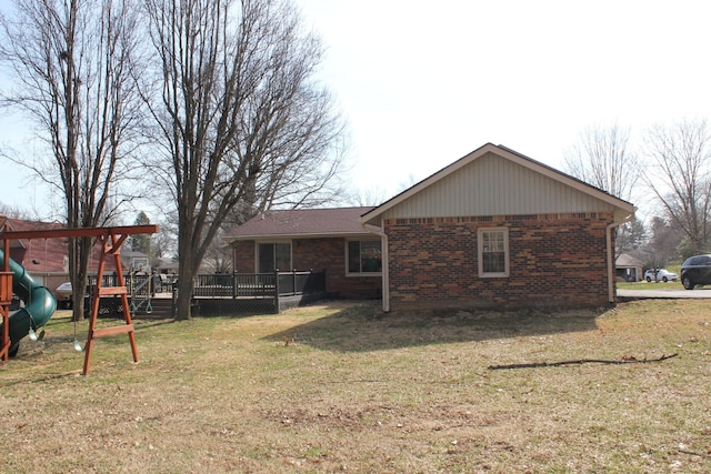 rear view of property with a lawn, a deck, brick siding, and a playground
