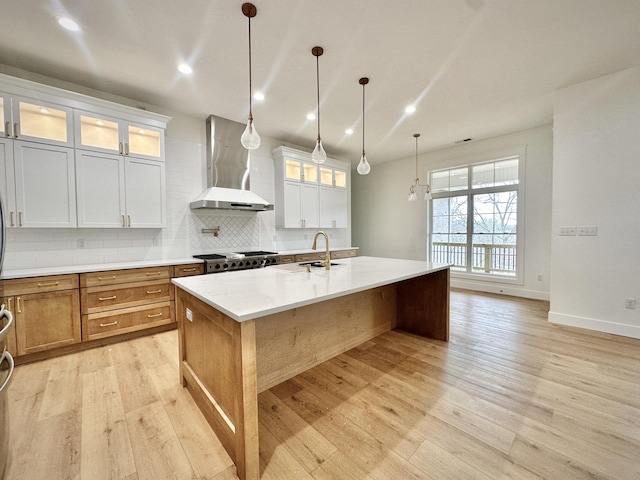 kitchen featuring light wood-style floors, backsplash, a center island with sink, and wall chimney range hood