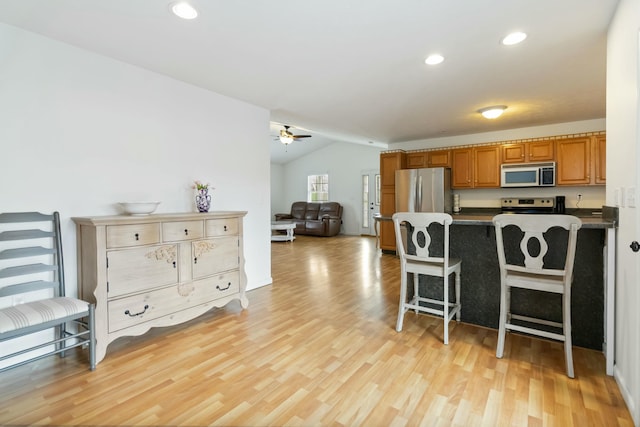 kitchen featuring ceiling fan, brown cabinets, dark countertops, appliances with stainless steel finishes, and vaulted ceiling