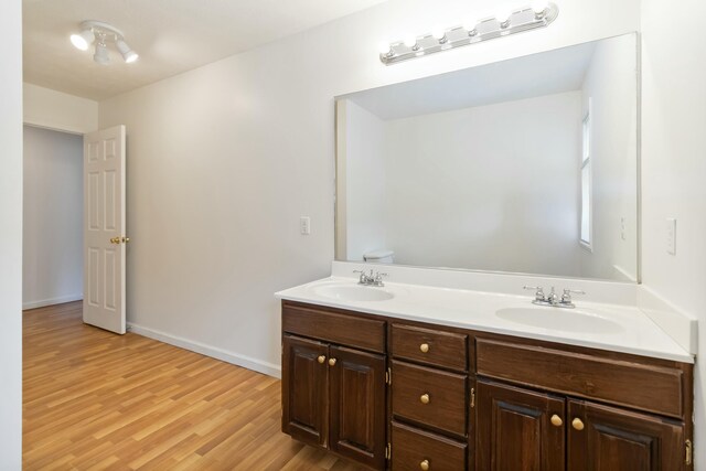 bathroom with double vanity, a sink, baseboards, and wood finished floors