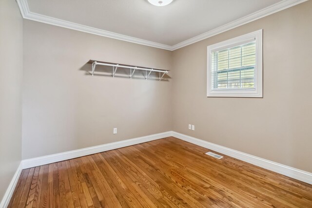 spare room with wood-type flooring, crown molding, baseboards, and visible vents