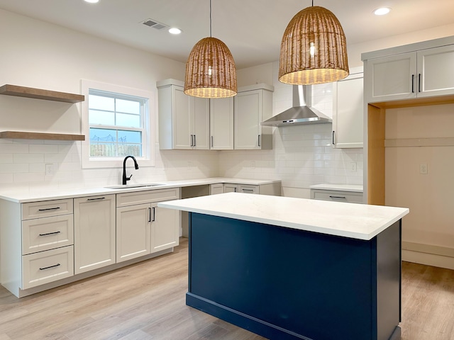 kitchen featuring tasteful backsplash, hanging light fixtures, a sink, light wood-style floors, and wall chimney exhaust hood