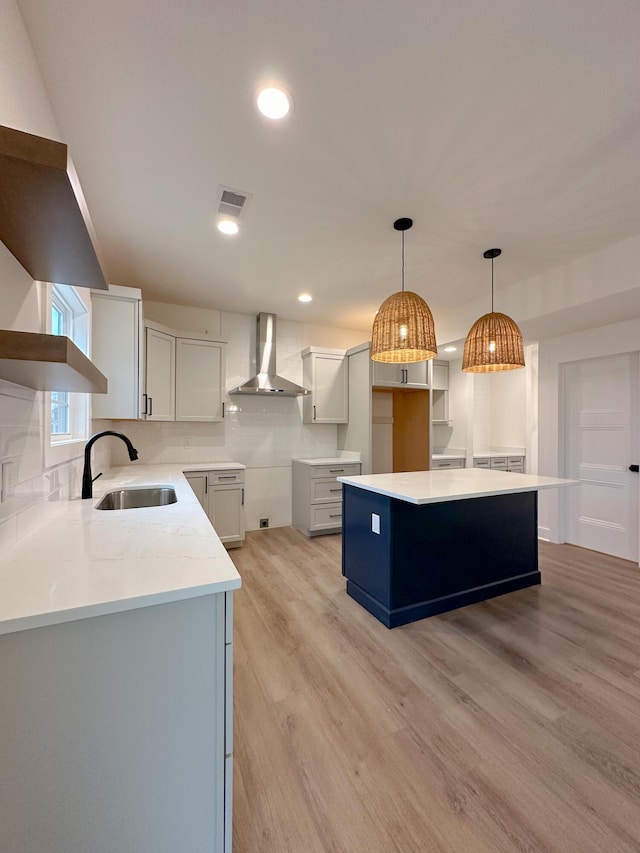 kitchen with backsplash, a sink, open shelves, wall chimney exhaust hood, and light wood-style floors