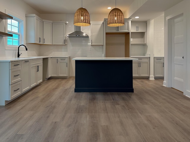 kitchen featuring backsplash, a sink, wood finished floors, hanging light fixtures, and wall chimney range hood