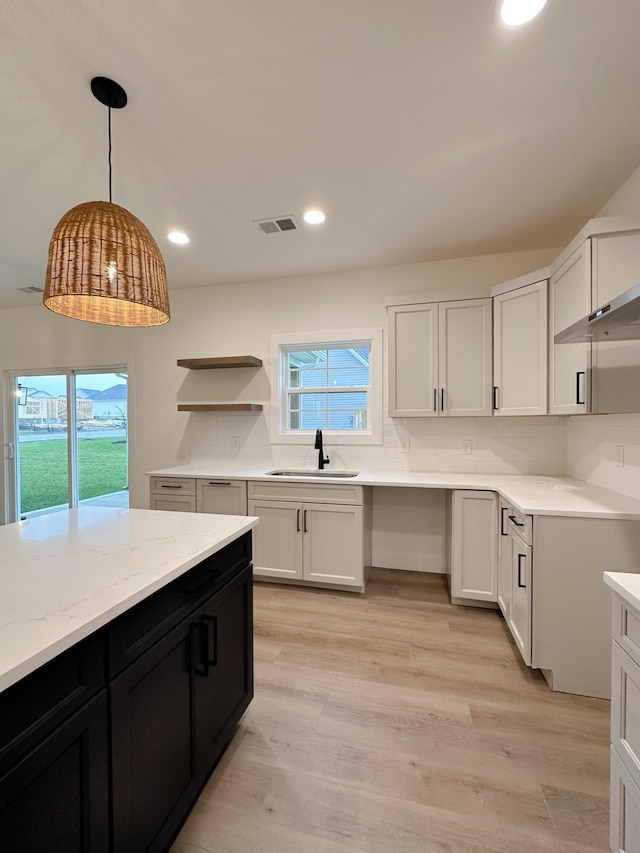 kitchen with a sink, open shelves, dark cabinetry, light wood-style flooring, and decorative backsplash