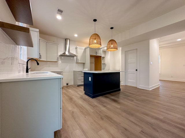 kitchen featuring decorative backsplash, visible vents, wall chimney exhaust hood, a sink, and light wood-style floors