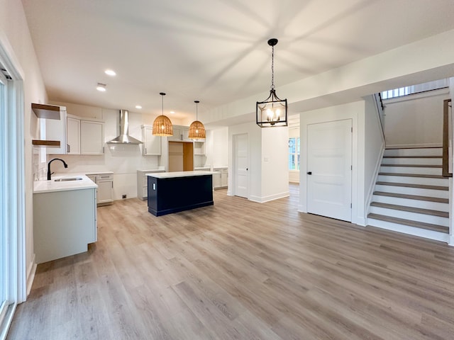 kitchen featuring white cabinets, a sink, light wood-type flooring, pendant lighting, and wall chimney range hood