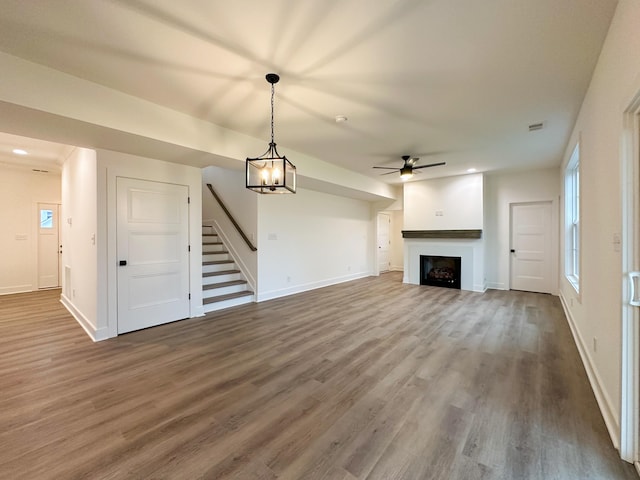 unfurnished living room featuring stairway, baseboards, ceiling fan, a fireplace, and wood finished floors