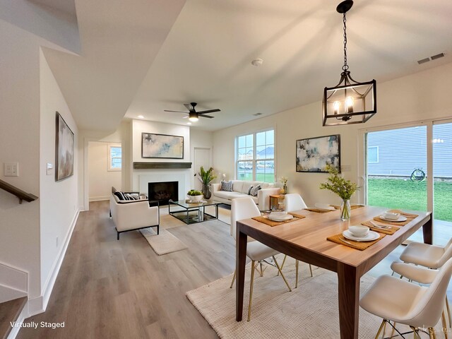 dining area featuring visible vents, baseboards, a fireplace, light wood-style floors, and ceiling fan with notable chandelier