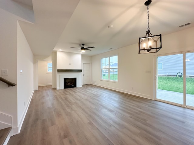 unfurnished living room featuring wood finished floors, ceiling fan with notable chandelier, baseboards, and visible vents