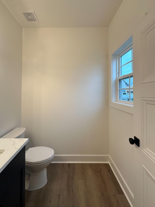 half bath featuring visible vents, baseboards, toilet, wood finished floors, and vanity