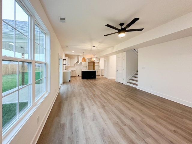 unfurnished living room with stairway, ceiling fan with notable chandelier, baseboards, visible vents, and wood finished floors