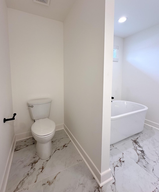full bathroom featuring baseboards, marble finish floor, toilet, a freestanding tub, and recessed lighting