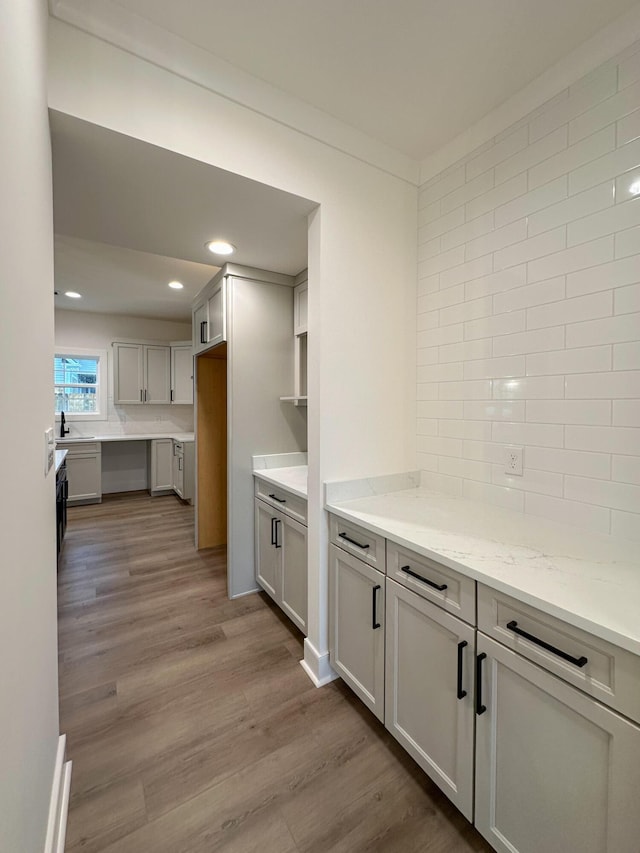 kitchen with backsplash, recessed lighting, light stone counters, and wood finished floors