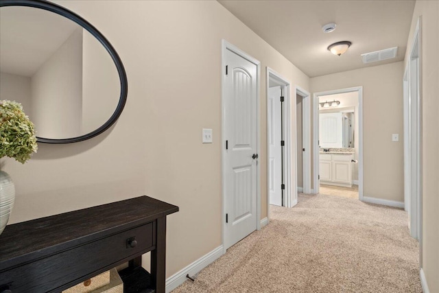 corridor featuring baseboards, visible vents, and light colored carpet