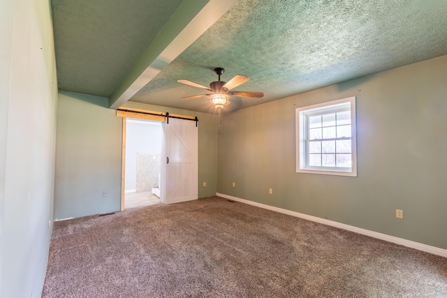 unfurnished bedroom featuring carpet flooring, baseboards, a barn door, and a textured ceiling