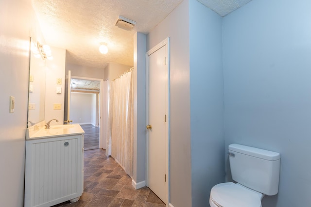 full bath with toilet, stone finish flooring, vanity, and a textured ceiling