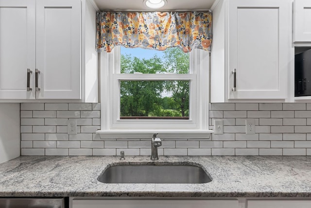 kitchen view of a sink, tasteful backsplash, white cabinets, and light stone counters