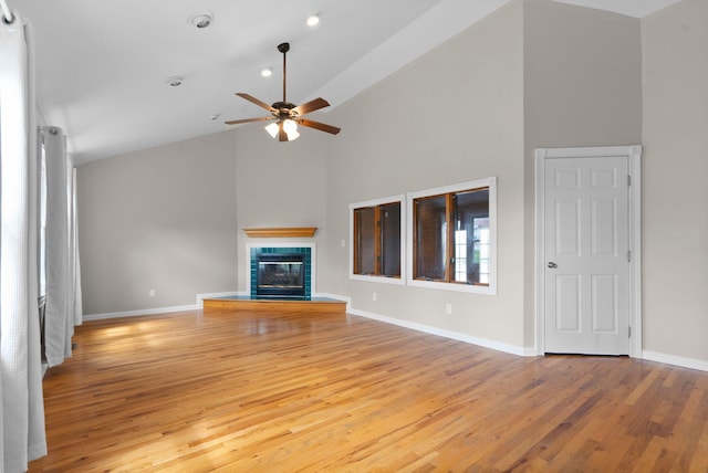unfurnished living room with ceiling fan, high vaulted ceiling, light wood-style flooring, a tiled fireplace, and baseboards