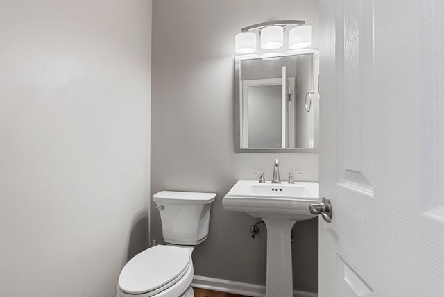 bathroom featuring toilet, baseboards, and a sink